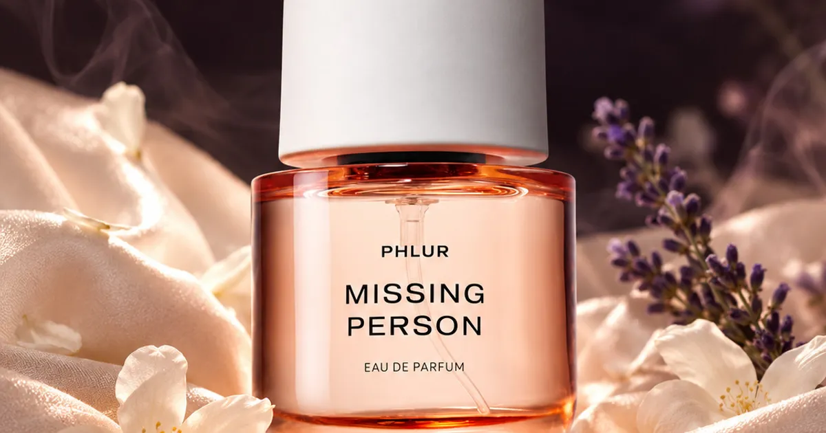 A soft pink perfume bottle resting on white silk with jasmine flowers and lavender.
