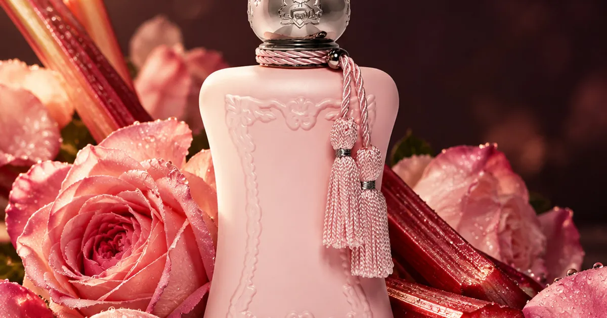 A pink perfume bottle surrounded by roses and rhubarb stalks in soft light.