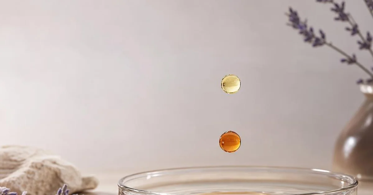 Two perfume droplets at different depths above a glass dish, with amber below and citrus above.